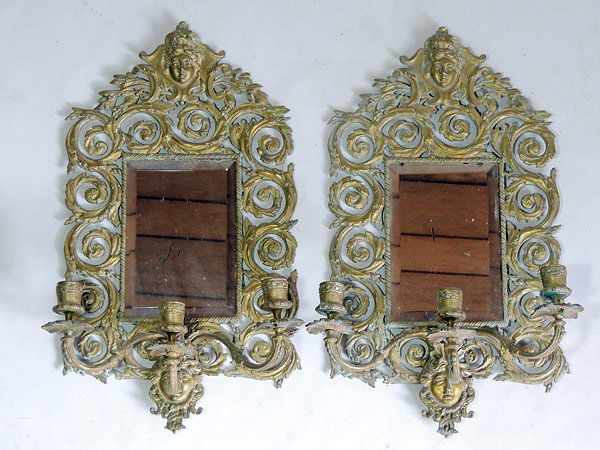 Pair of Cast Brass Girandoles: Pair of cast brass three light girandoles, with a face decorated crest and base, leaf scrolled surround, and beveled glass mirror inserts. 18-1/2” x 10”.