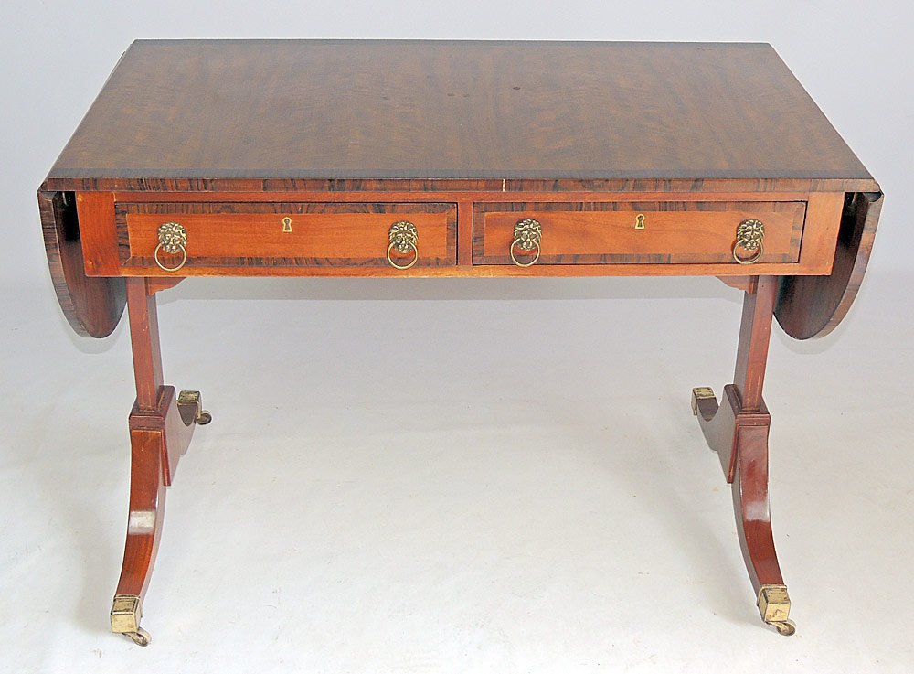 English Regency-style Sofa Table: English Regency-style mahogany sofa table with a banded rosewood rectangular top, with two half-circle drop-leaf ends and two frieze drawers, on swept sabre legs ending with brass castors. Size with l