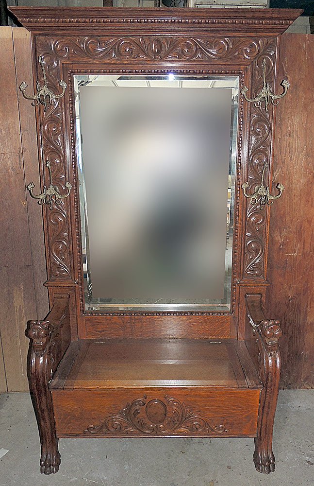 Carved Oak Hall Rack: Oak hall rack, featuring a heavily carved back with four fancy coat hooks, framing a large beveled glass mirror, lift top seat, lion mask arms, paw feet. 92" tall x 51" wide.