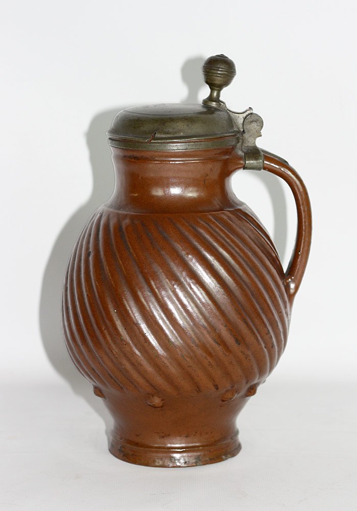 18th Century Redware Stein: Brown-glazed redware stein with pewter lid. Initialed "M.S." and dated 1760. Ball-shaped thumb piece, strap handle and twisted rib body. 10-1/2" tall x 7" wide.