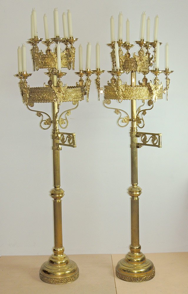 Pair of Brass Neoclassical Twelve-Light Torchieres: Pair of brass Neoclassical twelve-light torchieres. Each featuring two tiers of lighting and removable candleholders supported by winged putti. The lower superstructures are supported by scrolled foli