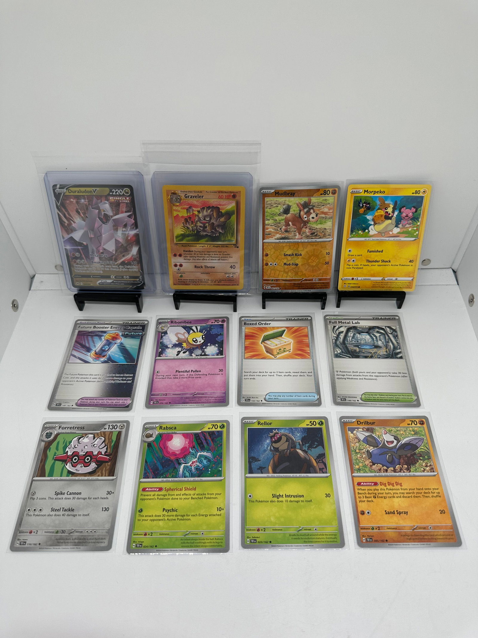 (12) TCG Pokemon V, Fossil vintage, Morpeko: * 12 various pokemon cards from various sets and years. * Add to your playing decks or complete your master sets. * Duraludon V * Graveler Fossil vintage * Mudbray Reverse Holo & Morpeko