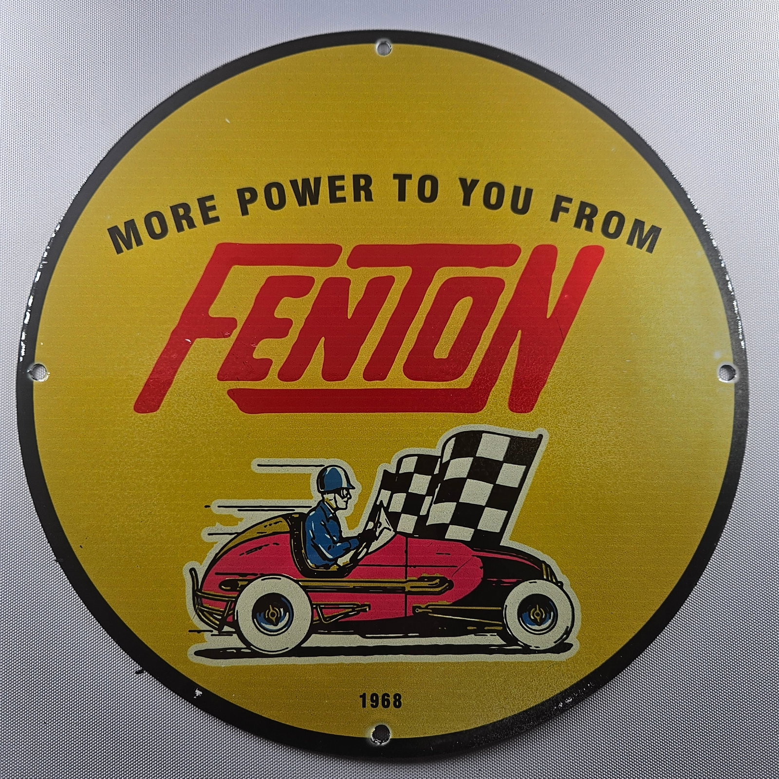 1968 More Power To You From Fenton 12-inch Porcelain Sign: The Fenton 12-inch porcelain sign is a captivating piece of advertisement history. Its vibrant design features bold red lettering that spells out “FENTON,” set against a golden b