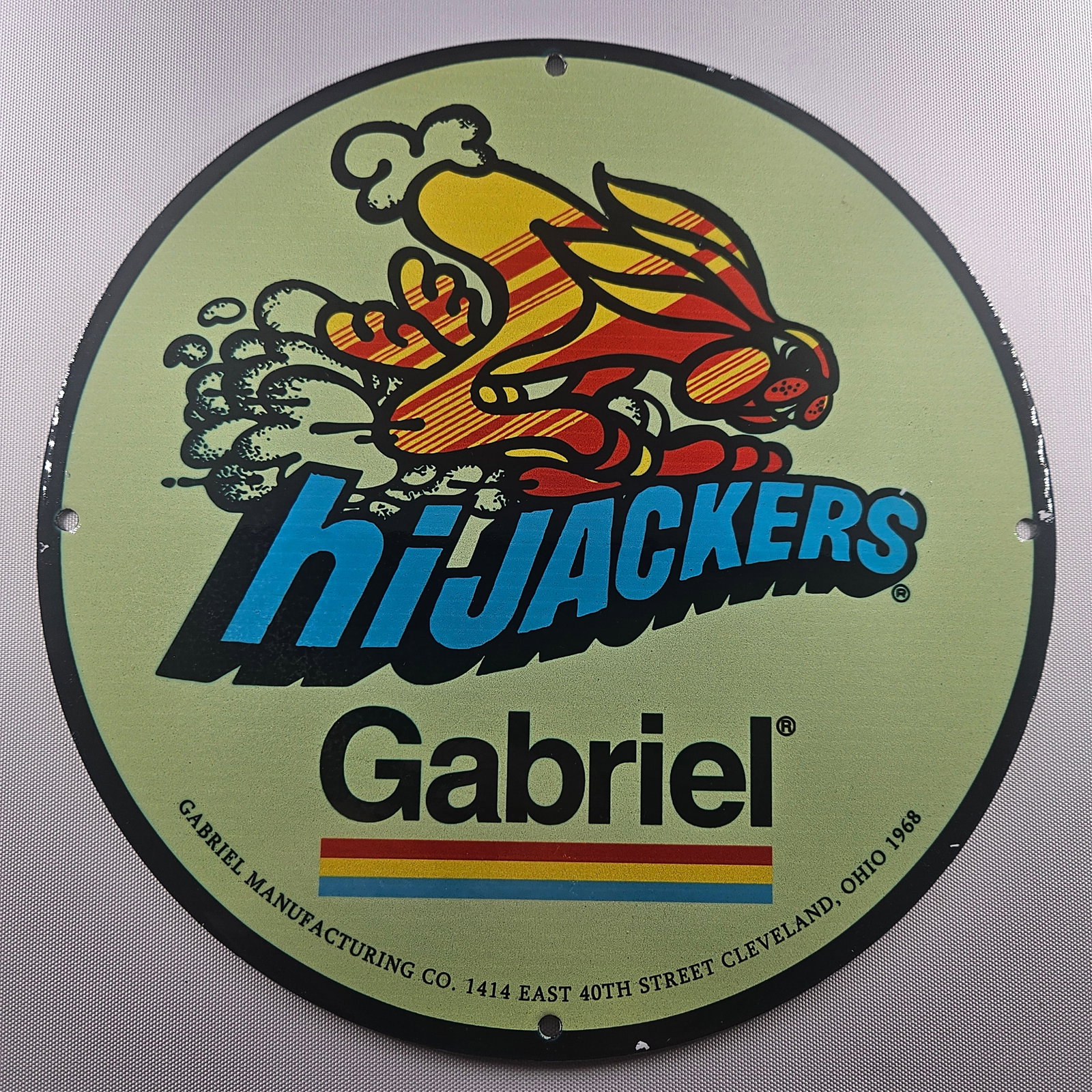 1968 hiJACKERS by Gabriel Manufacturing Co. 12-inch Porcelain Sign: The 1968 hiJACKERS by Gabriel Manufacturing Co. 12-inch Porcelain Sign is a captivating piece of advertisement history, showcasing the distinctive hiJACKERS logo. Measuring 12 inches in diameter, this