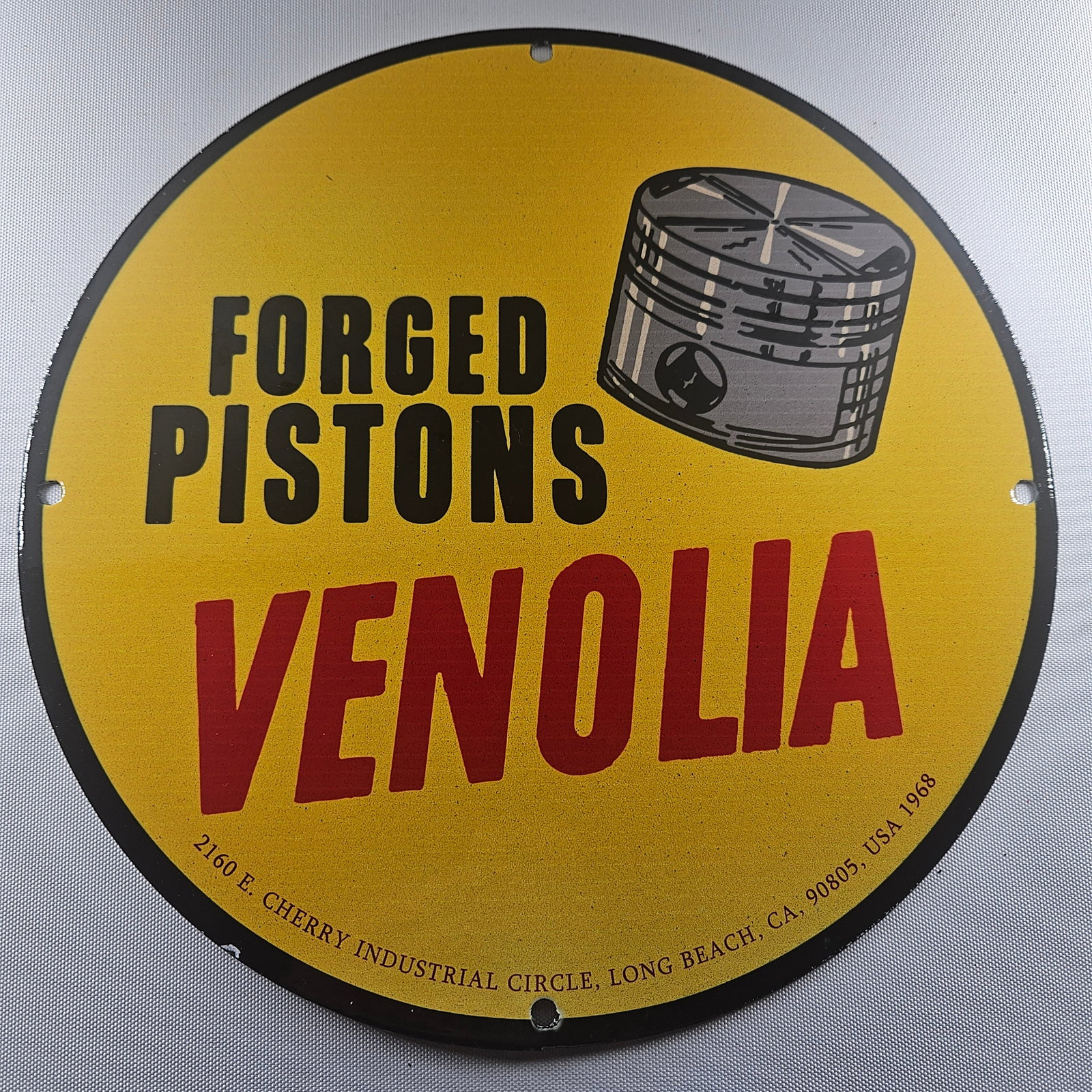 1968 Venolia Forged Pistons 12-inch Porcelain Sign: The 1968 Venolia Forged Pistons 12-inch Porcelain Sign is a captivating piece of advertisement history, showcasing the distinctive Venolia logo. Measuring 12 inches in diameter, this sign represents t