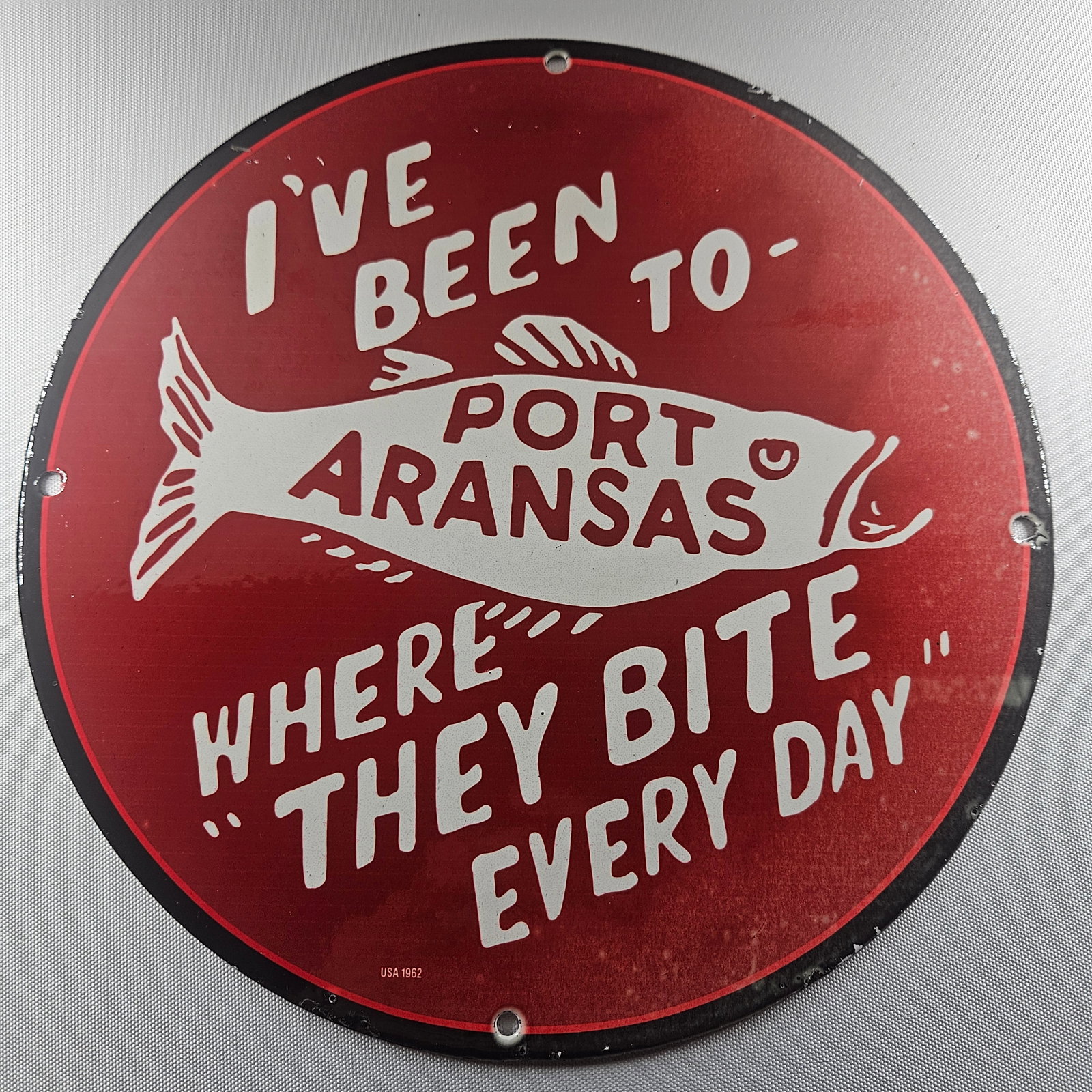 1962 Port Aransas Fishing 12-inch Porcelain Sign: The 1962 Port Aransas Fishing 12-inch Porcelain Sign is a captivating piece of advertisement history, celebrating the rich heritage of fishing in Port Aransas. Measuring 12 inches in diameter, this si