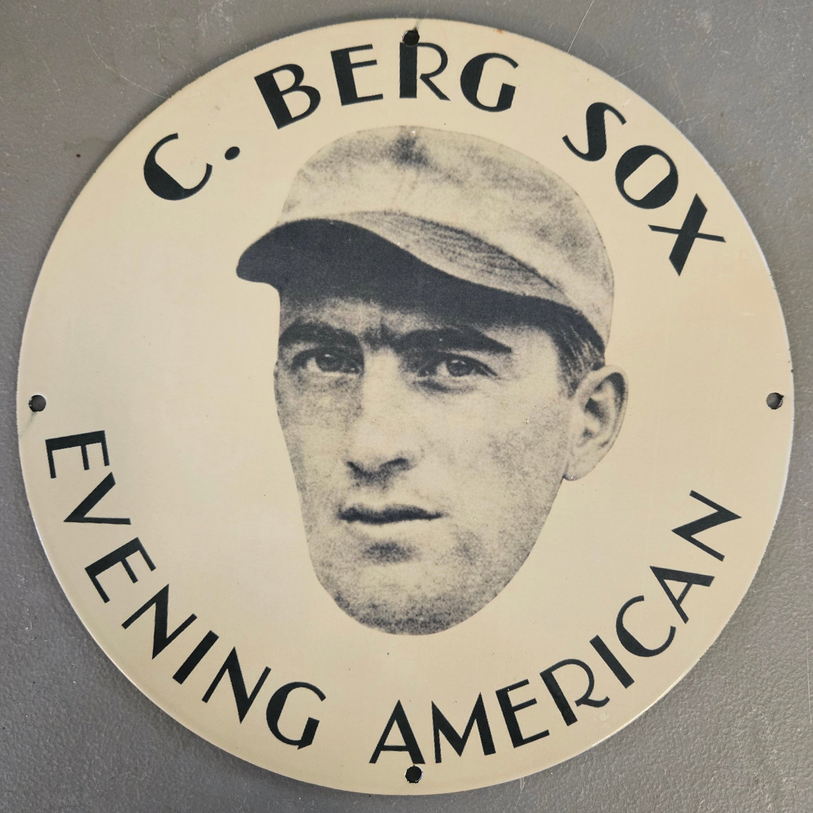 C. BERG SOX EVENING AMERICAN 12" PORCELAIN BASEBALL SIGN: 12-inch round porcelain enamel baseball sign featuring an early ballplayer portrait surrounded by bold “C. BERG – SOX – EVENING AMERICAN” lettering. The simple black-and-cream design gives