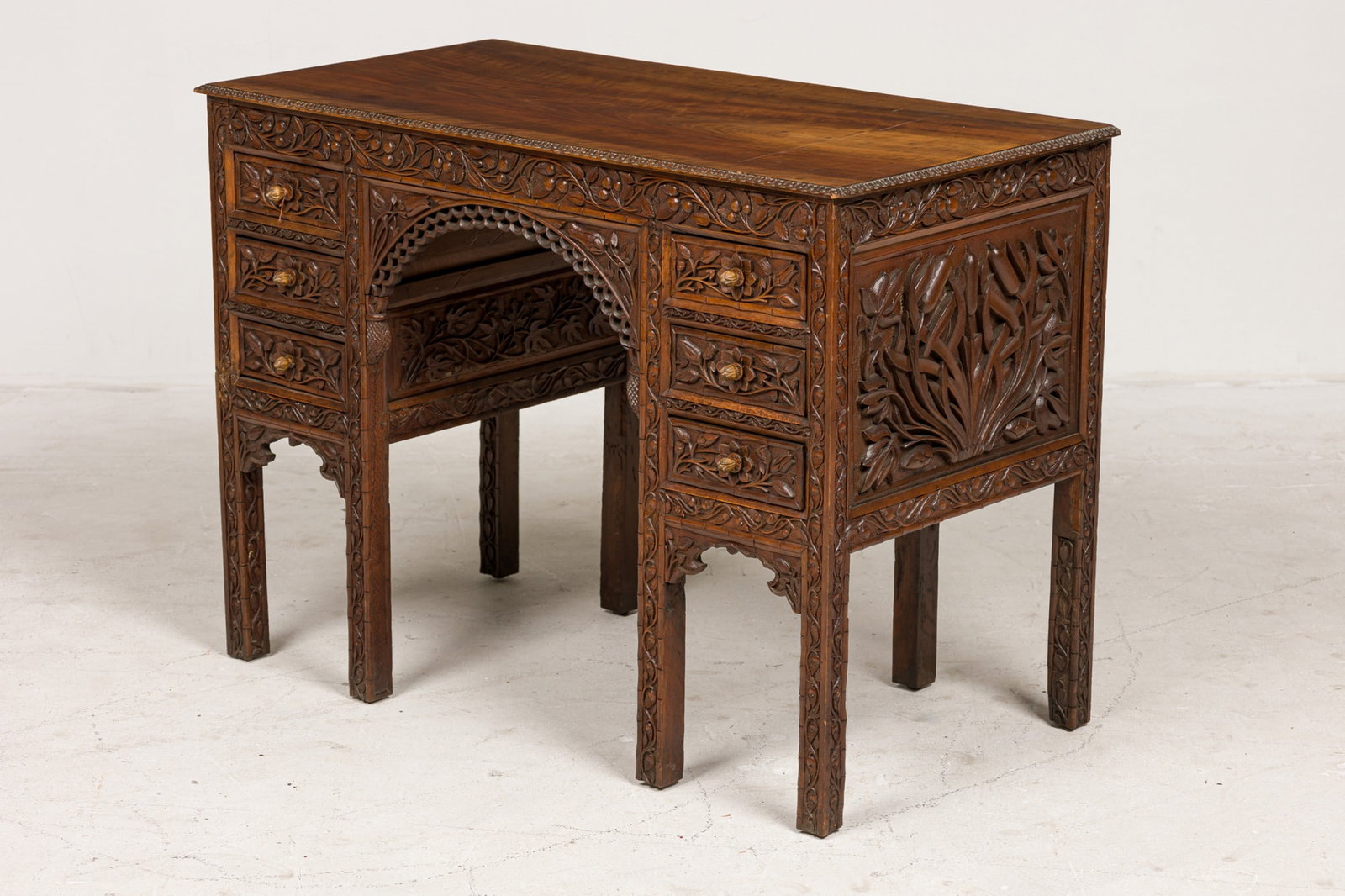 Anglo-Indian Floral Carved 5-Drawer Teak Desk: 19th/20th c., India, carved teak, the whole intricately decorated with leaf & floral carving, the arched kneehole centered between banks of drawers, 42"l x 21.25"d x 30.25"h
