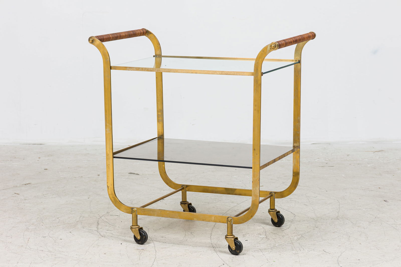 Carl Aubock, Brass Two-Tier Bar Cart: c. 1950s, Austria, tinted and clean glass shelves, rattan-wrapped handles, 28.5"h x 27"l x 17"d Provenance: A Private Collection: 36 Gramercy Park E