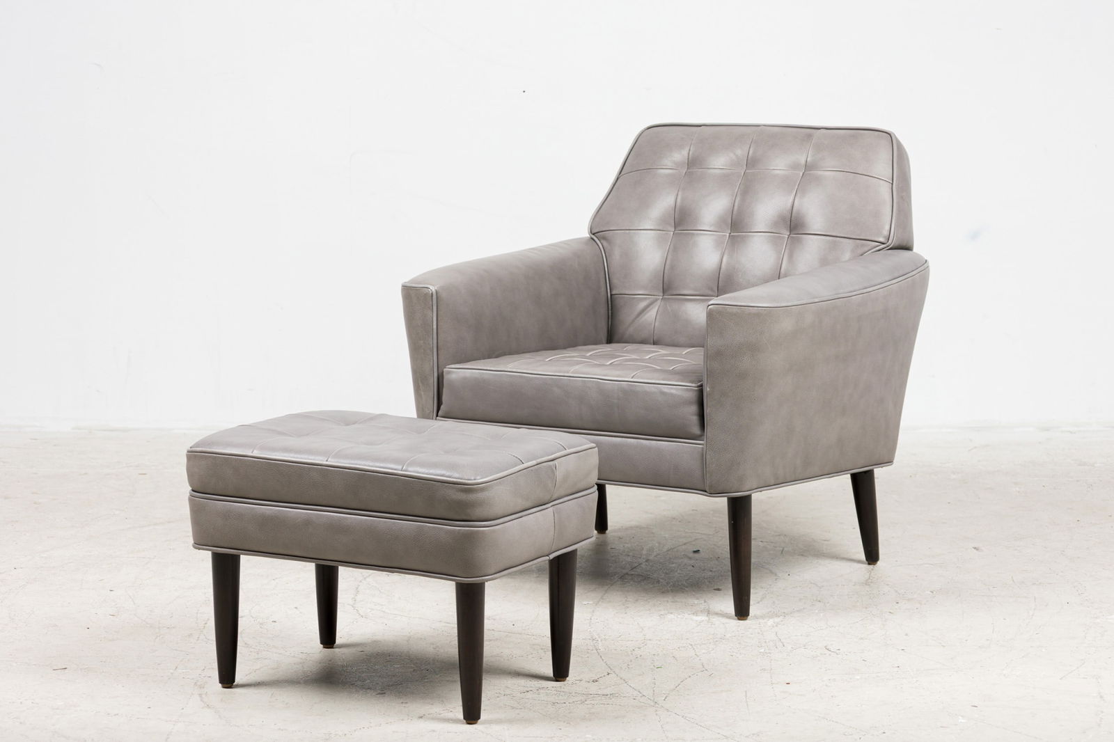 Custom Modern Leather Club Chair And Ottoman: 21st c., USA, button-tufted back and loose seat cushion, fully upholstered in grey leather, with round tapering legs, designed or sourced by Bunny Williams Interiors, 30"h x 30"w x 33"d
