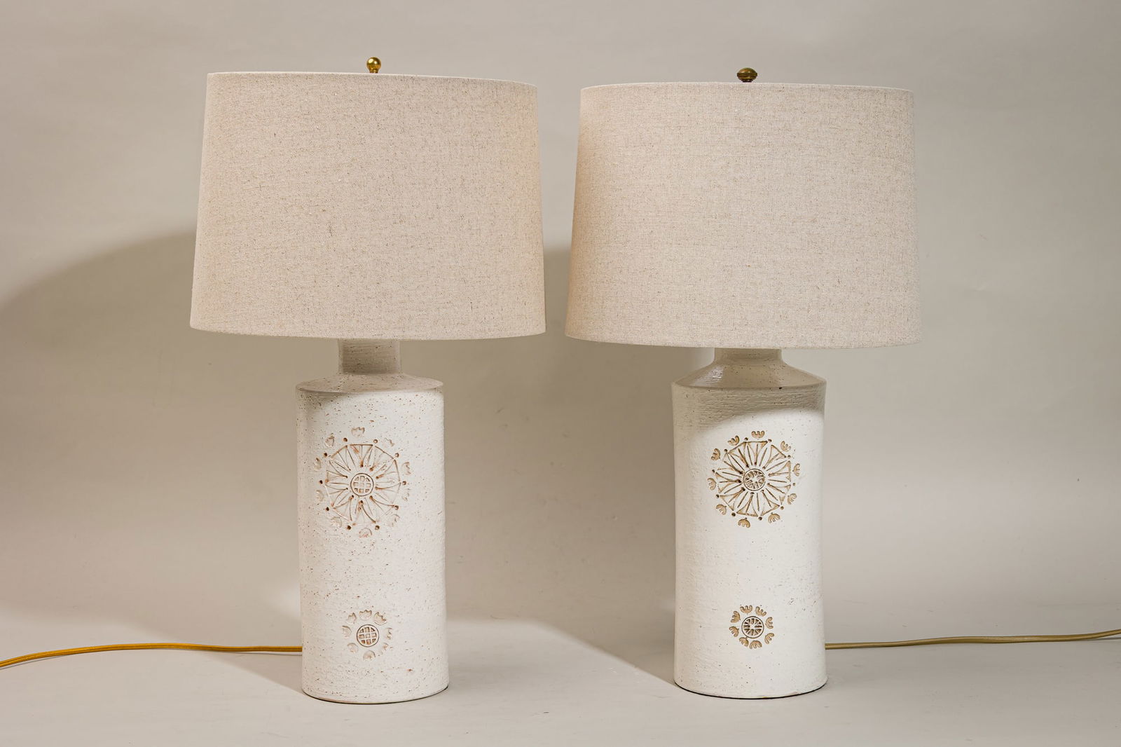 Aldo Londi for Bitossi, pair ceramic table lamps: c. 1960s/1970s, Italy, textured white glaze with impressed geometric designs, fabric shades, "BERGBOMS" sticker underside, 21.75"