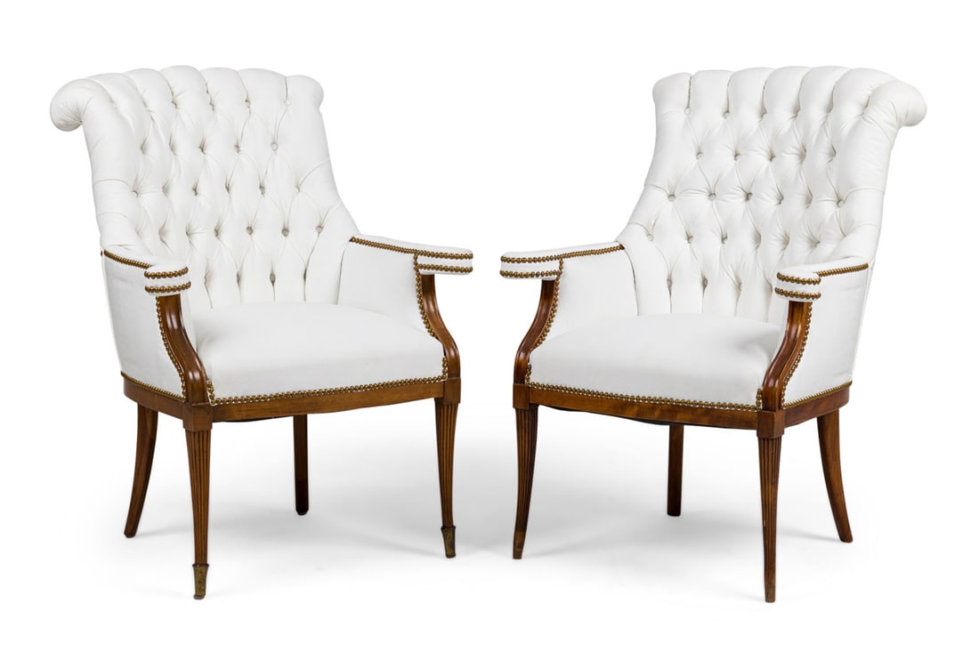 Grosfeld House style, pair white tufted armchairs: 20th c., USA, the padded seat, armrests and back upholstered in white tufted faux leather, with scrolling headrest and arm supports, on fluted legs ending in brass sabot (on chair lacking), 39" h x28"