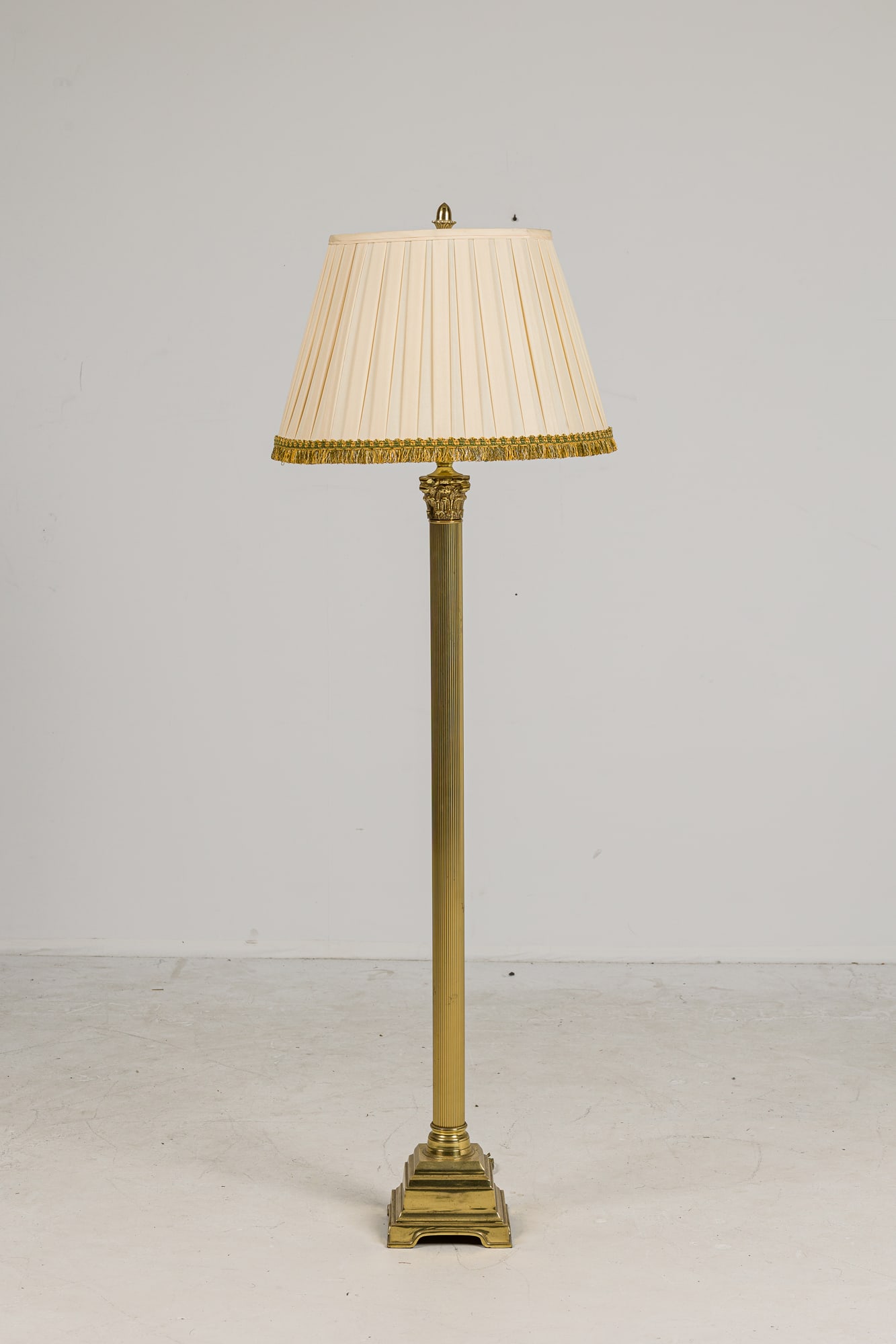 Neoclassical style floor lamp with pleated silk shade: 20th c., USA, brass fluted column stem with acanthus leaf design, mounted on a stepped base, with silk pleated shade trimmed in a green and gold fringe, 64.25"h x 7.5"dia. Provenance: From a Mac II de