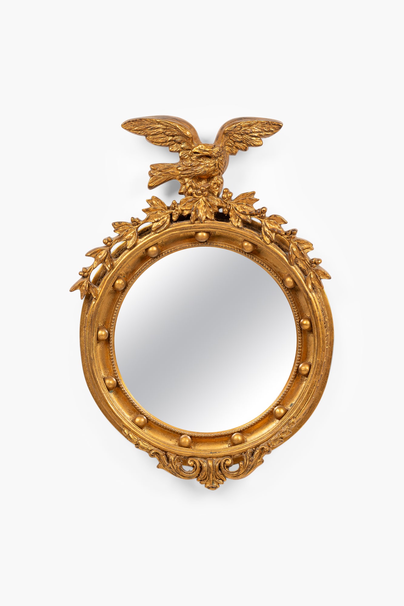 American Federal style gilt mirror: 20th c., gold finished composite, surmounted by an eagle clutching a breach laden with berried, the circular frame decorated with multiple spheres, 33"h x 23"wProvenance: 465 Park Ave