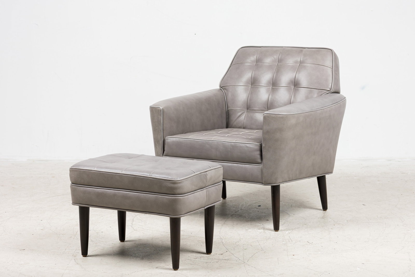 Custom modern leather club chair and ottoman: 21st c., USA, button-tufted back and loose seat cushion, fully upholstered in grey leather, with round tapering legs, designed or sourced by Bunny Williams Interiors, 30"h x 30"w x 33"d (chair), 15"h
