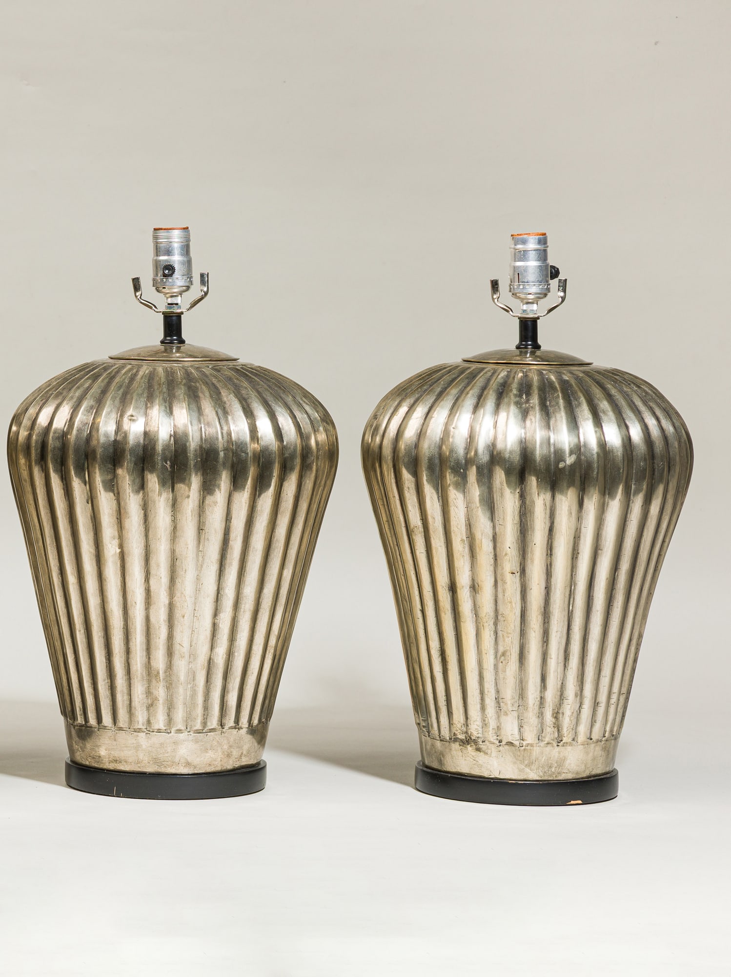 Pair modern ribbed metal lamps: mid-20th c., silver finished metal, vertical fluted urn shape, contrasting black painted wooden base, 18.25"h x 10.5"dia.Provenance: 465 Park Ave