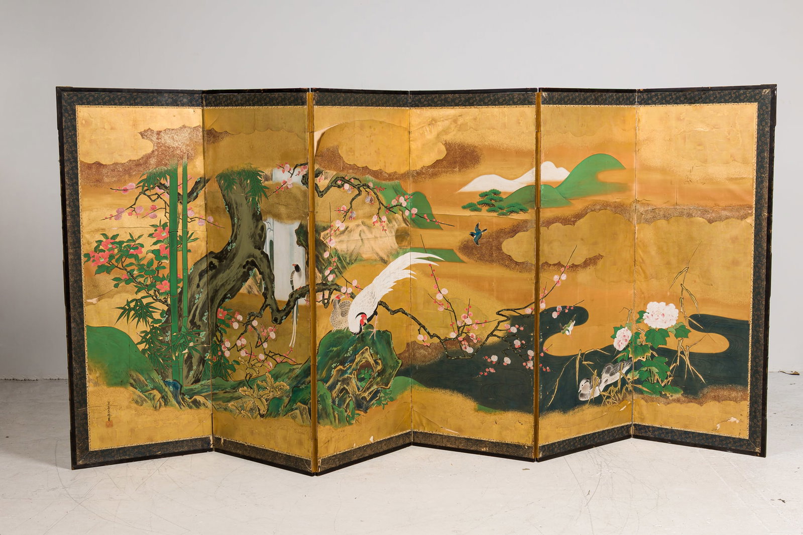 Kano School, Large Edo Period six panel screen, ex Sotheby's: Edo Era (17th-19th c.), Japan, Ink, colors, gofun and gold leaf on paper, depicting a blossoming Prunus, bamboo, Camellia, and a pair of roosters on a ground of gold swirling clouds dotted w