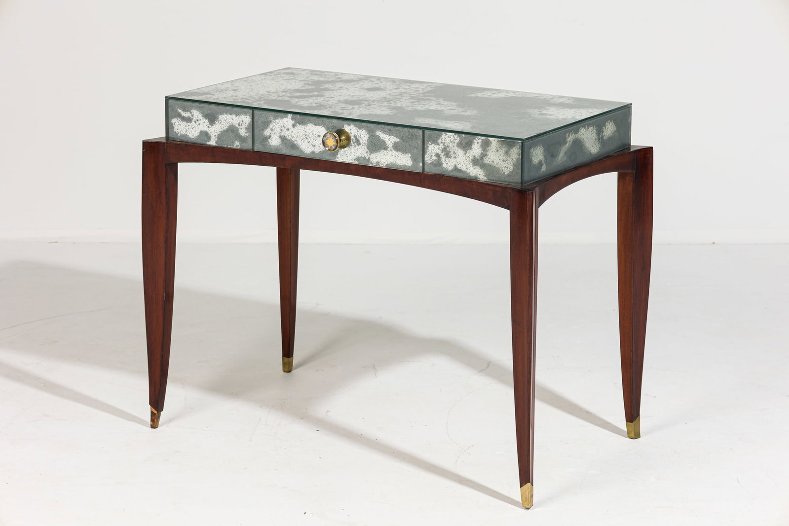 French Art Deco mirrored mahogany writing table: c. 1940s, France, mahogany frame with curved tapered legs ending in brass sabots, antique mirror paneled top, the single frieze drawer set with star-patterned knob, 28.5" h x 37" w