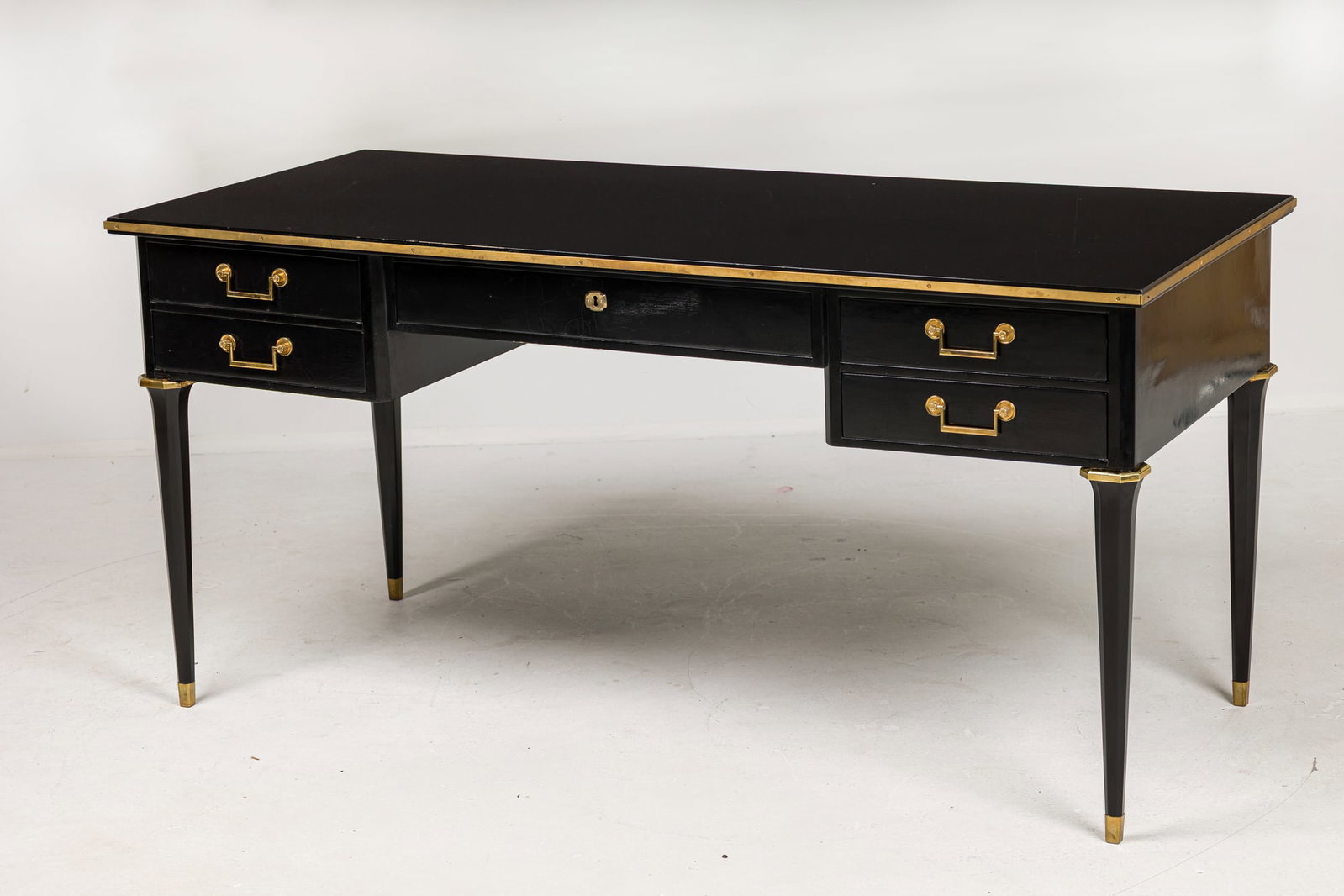 Maison Jansen (attrib) French Louis XVI style bureau plat: c. 1940s, France, ebonized piano lacquered finish, the center frieze drawer flanked by two stacked drawers on each side, gilt bronze hardware, raised on octagonal tapered legs endi