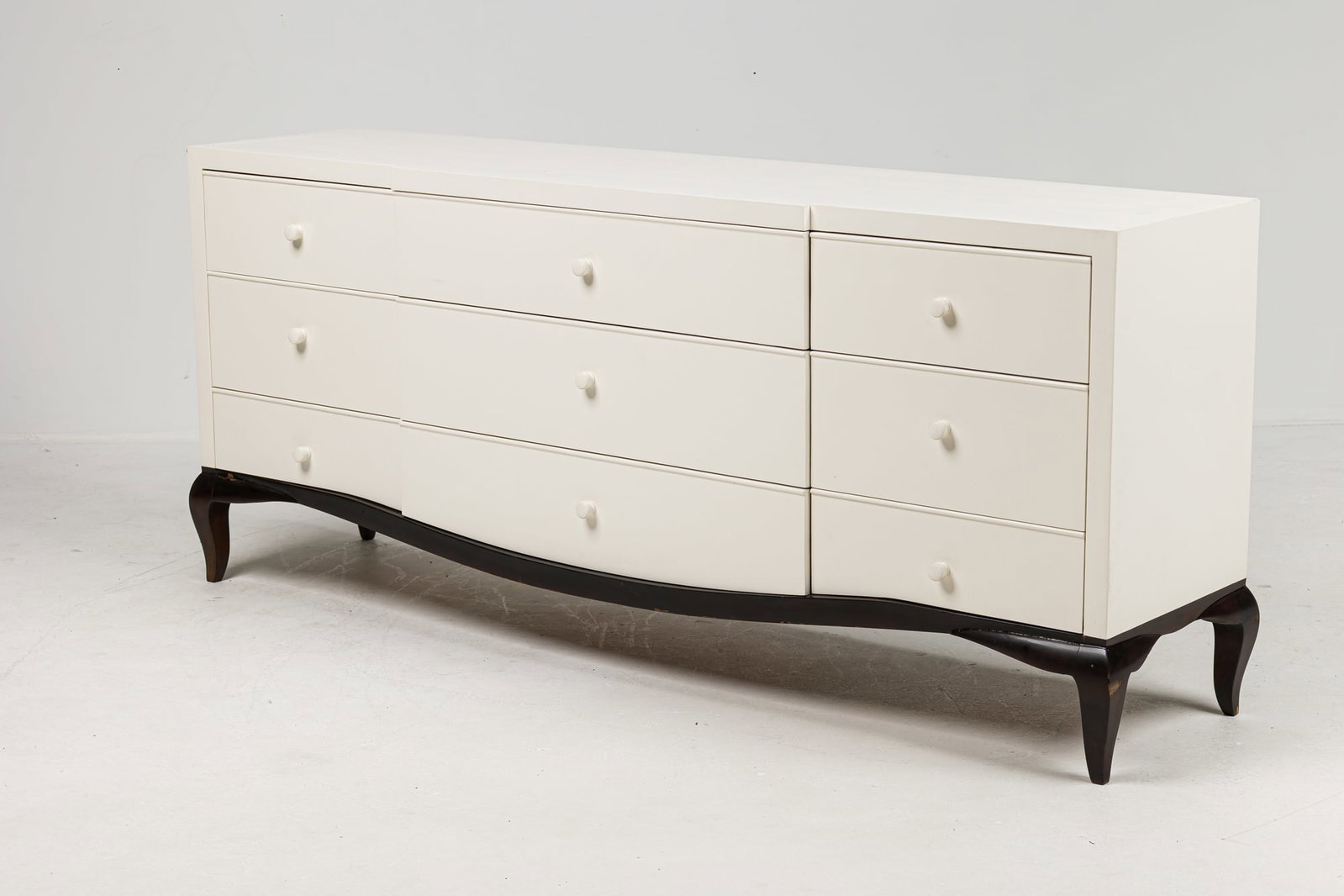 Contemporary Art Deco style cabinet, Stephen Bastone: 21st c., USA, white painted wood cabinet, set with nine drawers, with wooden knobs, rests on black lacquered base with curved legs, 31.25" h x 74.5" w x 16.5" d Provenance: Property fro