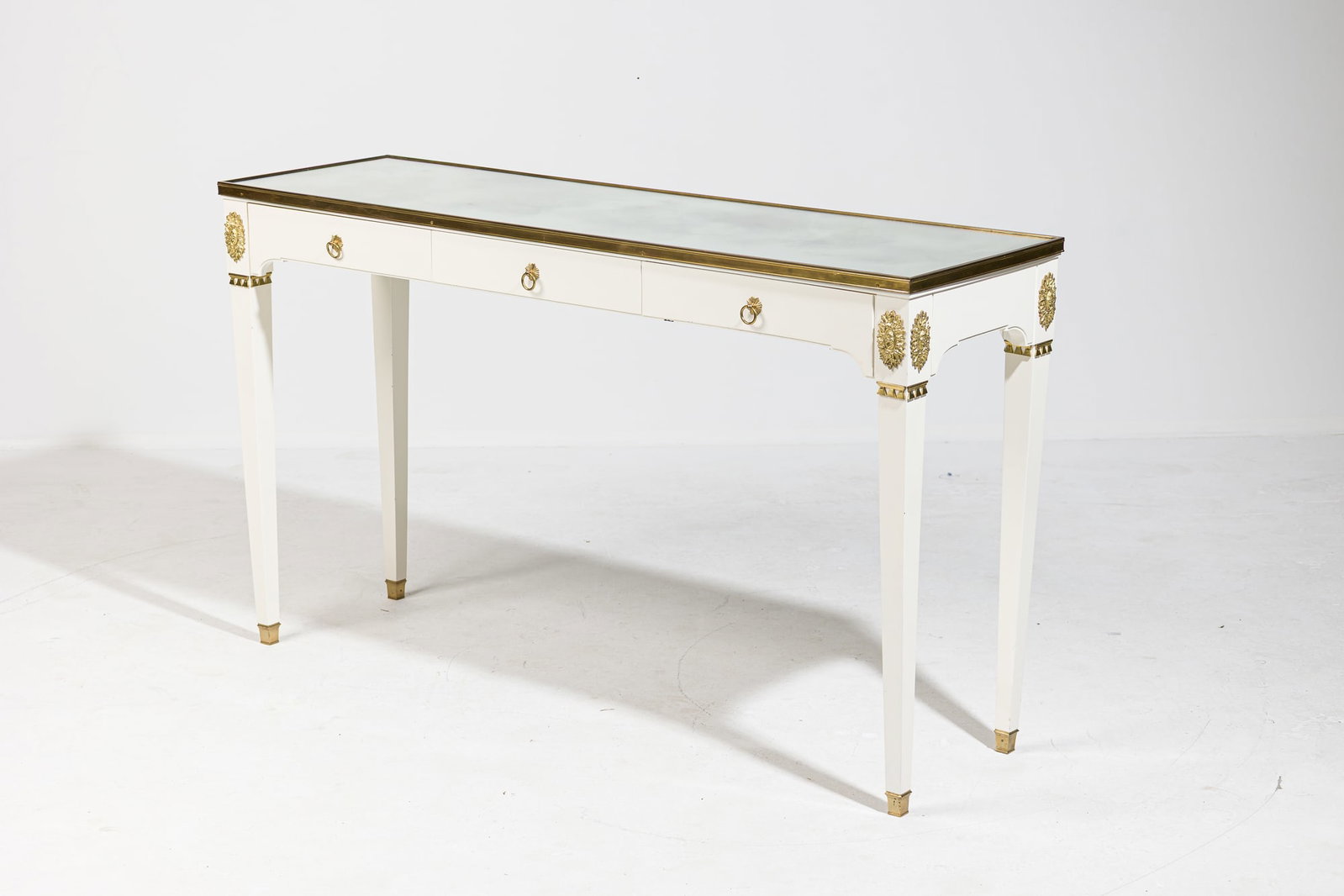 Maison Jansen (style), Neoclassical mirrored and ormolu mounted console: mid-20th c., France or Italy, cream lacqurered wood frame mounted with cast gilt bronze medallions and banding, the rectangular mirrored glass top framed in gilt brass, over three frieze dra