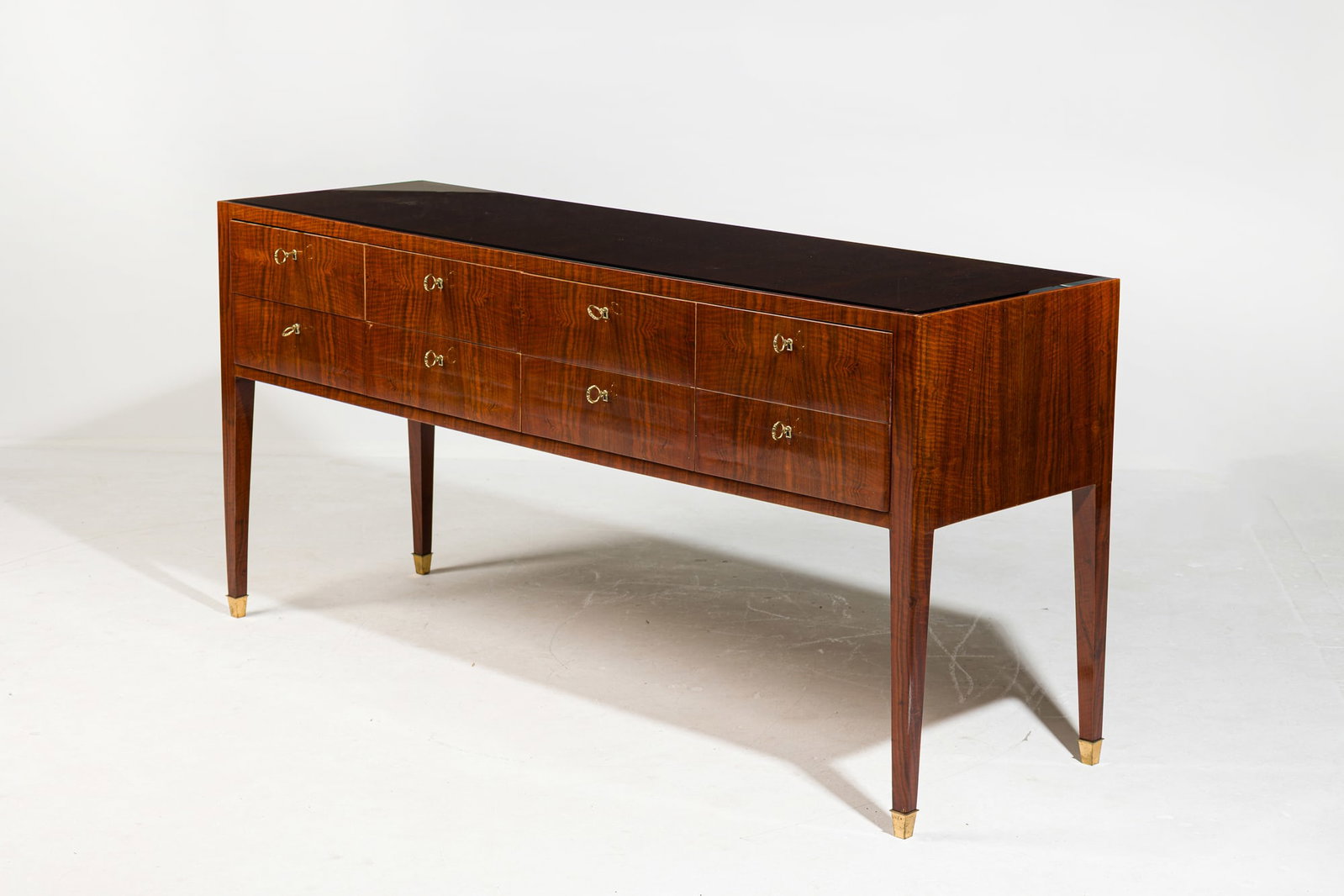 Paolo Buffa, Fine Italian Modern eight drawer sideboard: c. 1940s, Italy, highly figured dappled Italian Walnut veneer, with clear inset glass top, the 8 drawers each set with brass escutcheon and working lock, raised on tall slende