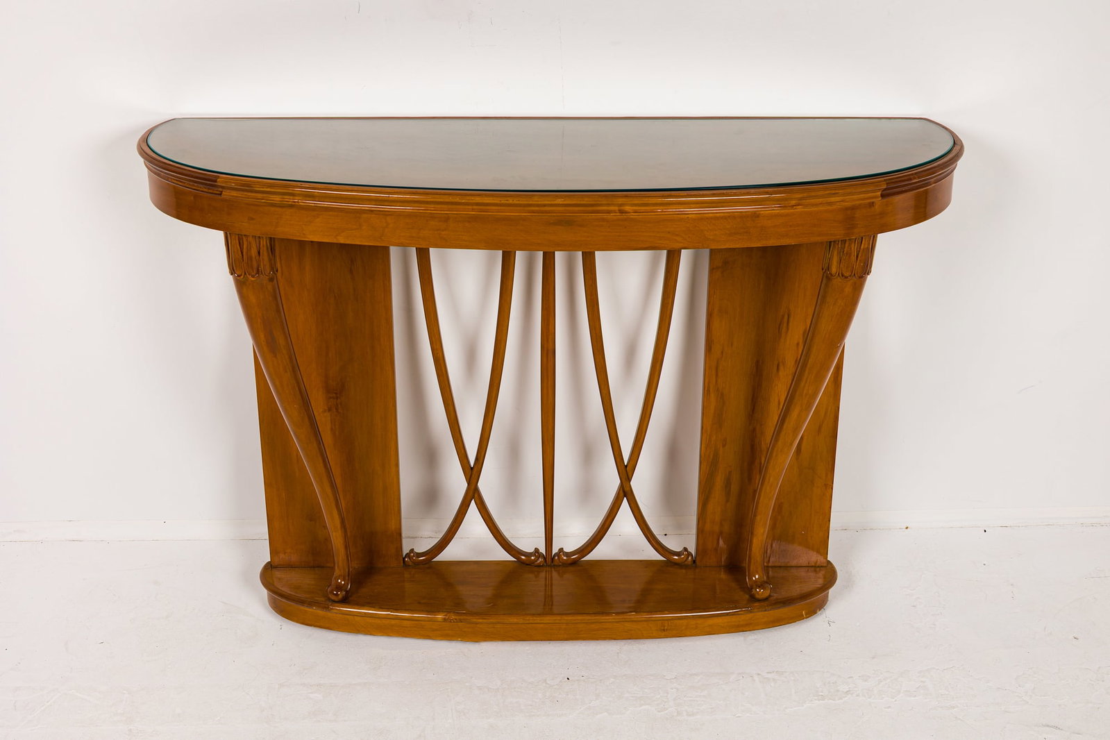 Osvaldo Borsani (attrib), Italian Modern wall-mounted demi-lune console: c. 1940s, Italy, carved fruit wood, inset glass top, raised on cornucopia form supports, 38.5" h x 55" w x 17.75" d Provenance: Property from 502 Park Ave: A Stephen Bastone bespok