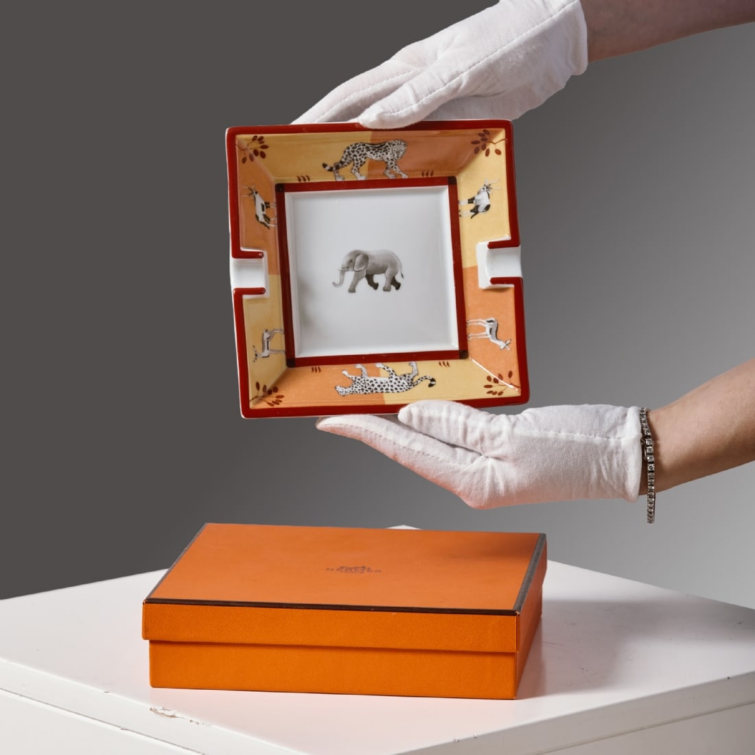 Hermes Porcelain Ashtray, Africa Model, in Orange Tones: Hermes Porcelain Ashtray, Africa Model, in Orange Tones, in earth-orange tones with African animal decorations and an elephant in the center. Comes in the original box. Condition: Light signs of use. 