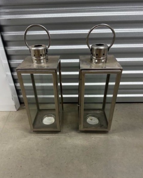 Pair of Modern Metal Lanterns: A pair of sleek, modern metal lanterns featuring a polished finish and glass panels. Each lantern has a round handle on top for easy carrying or hanging. Ideal for both indoor and outdoor use, these l