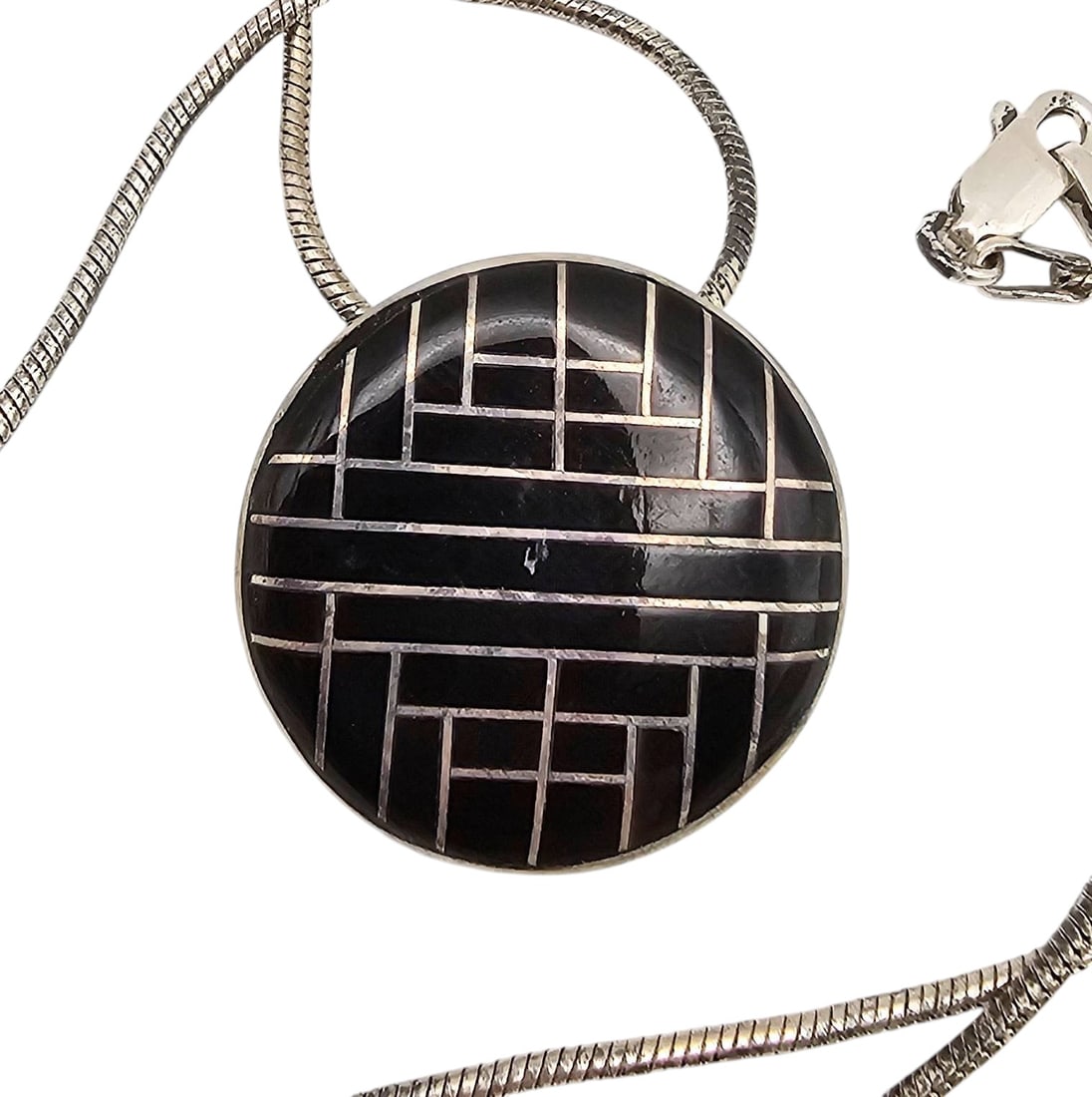 Native Onyx Inlay Sterling Necklace: Sterling silver necklace featuring a round pendant with a native onyx inlay in a geometric design. The pendant measures approximately 1.5 inches in diameter. The snake-style chain is stamped ‘STERLI