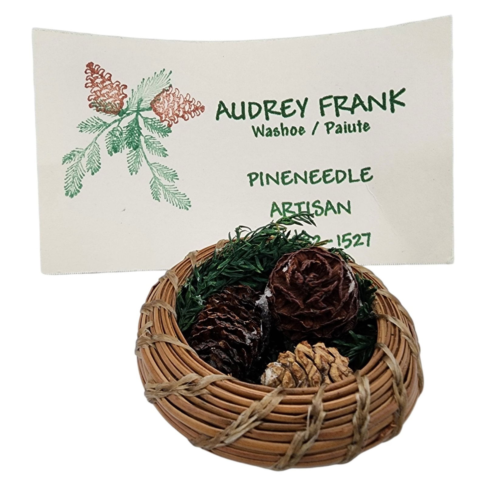 Native American Pine Needle Basket by Audrey Frank, Washoe/Paiute Tribe: Native American Pine Needle Basket by Audrey Frank, Washoe/Paiute Tribe / 6g / .5"h x 1.8"d / Note: one of the pinecones is loose, comes with artist's card from time of purchase. Please familiarize