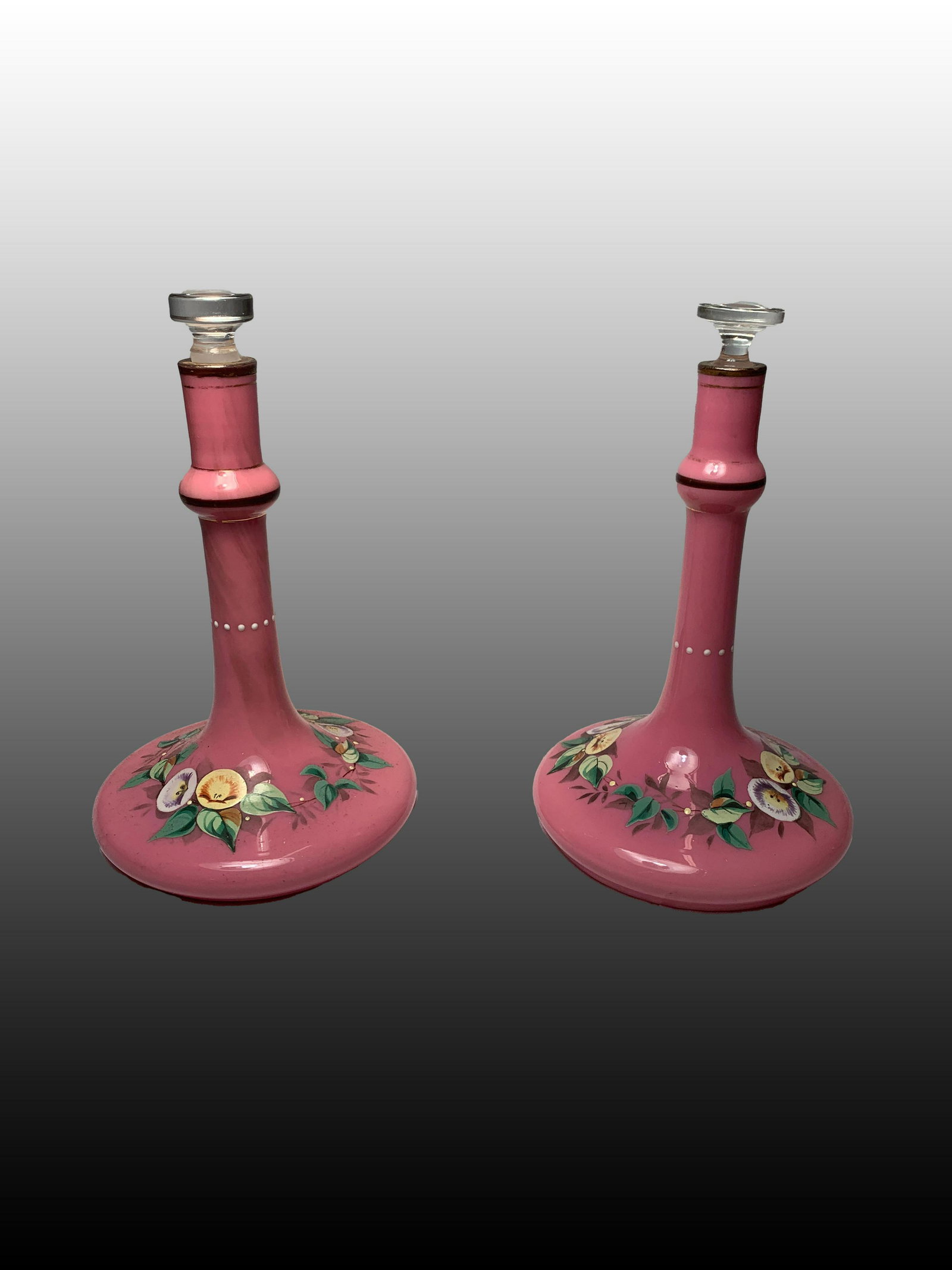 Pair of Pink Opaline Perfume Bottles: Early 20th c pair of pink opaline glass perfume bottes with glass stoppers, and painted with floral decorations. Each one measures 6 3/4 x 4 inches.