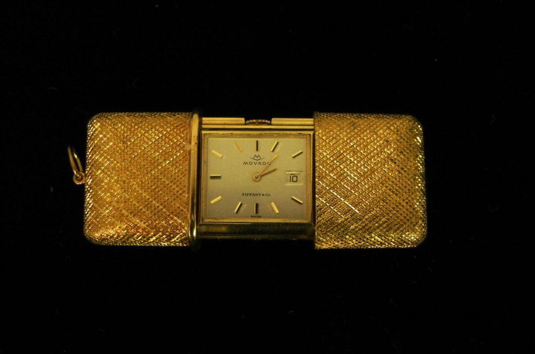 18KYG Tiffany & Co. Travel Clock: 18KYG Tiffany & Co. travel clock with Movado movement. The textured case of the clock slides open to reveal a rectangular white dial with gold chapters, aperture for date within a yellow gold case num
