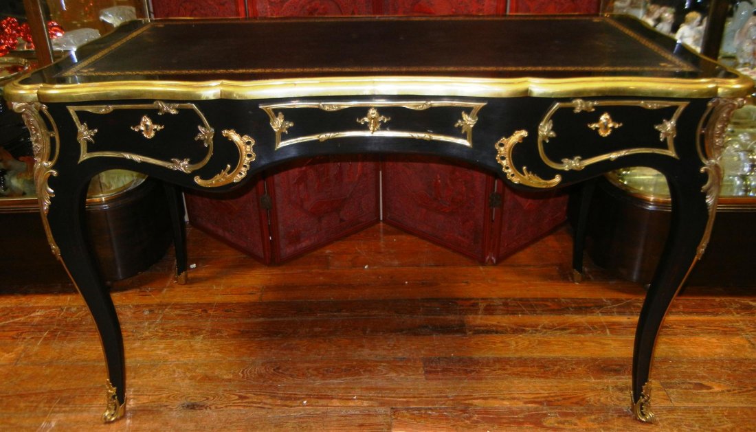 20thc. Louis XV Style Desk: Louis XV style desk with gold plated ormolu and black lacquered finish. Desk has a black leather top with gold tooling. Desk is outlined with scrolled ormolu on apron. Knee of leg embellished with aca