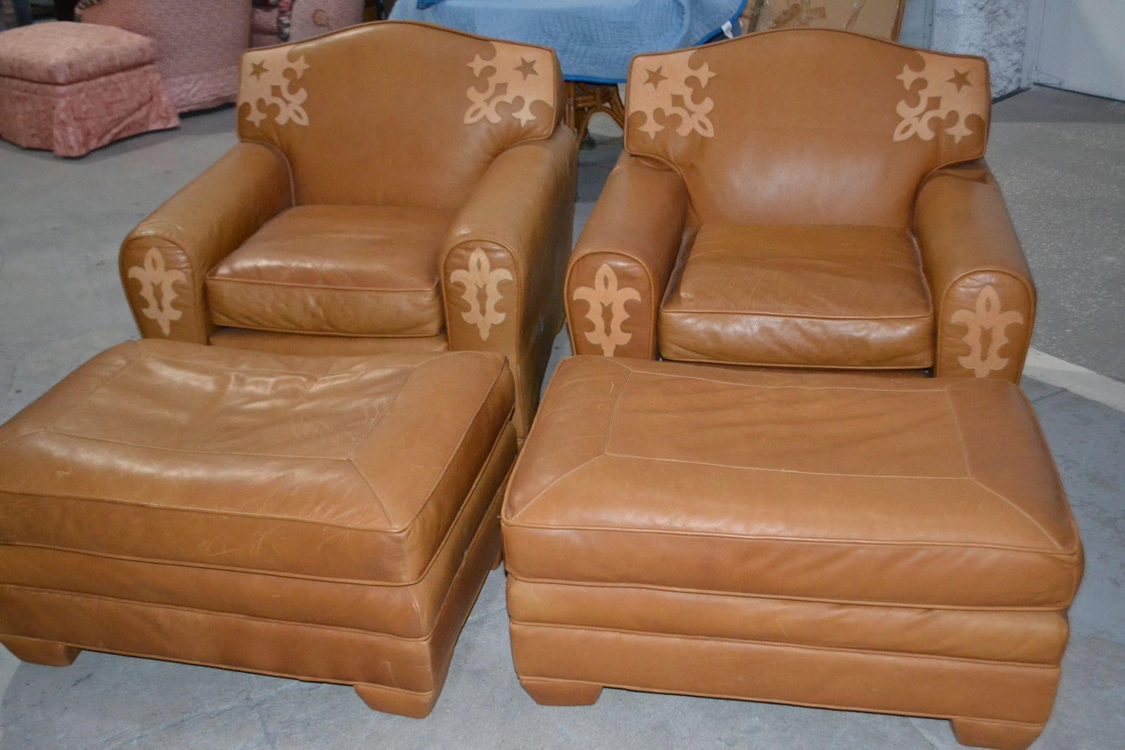 LENORE MULLIGAN (2) LEATHER CHAIRS & (2) OTTOMANS: LENORE MULLIGAN DESIGNS (2) LEATHER CHAIRS and (2) OTTOMANS TAN WESTERN STYLE FLEUR DE LIS Cowboy Collection Designers come look! resembles a wolf in center at arms and star on corners of chair back.