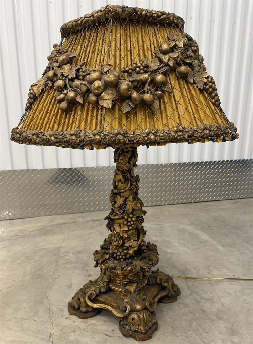 Ornate Table Lamp and Shade carved gilded base: Ornate table lamp featuring a carved, gilded base adorned with fruits and foliage, reminiscent of Baroque or Italianate styles. The base appears to be carved wood or composition material finished with