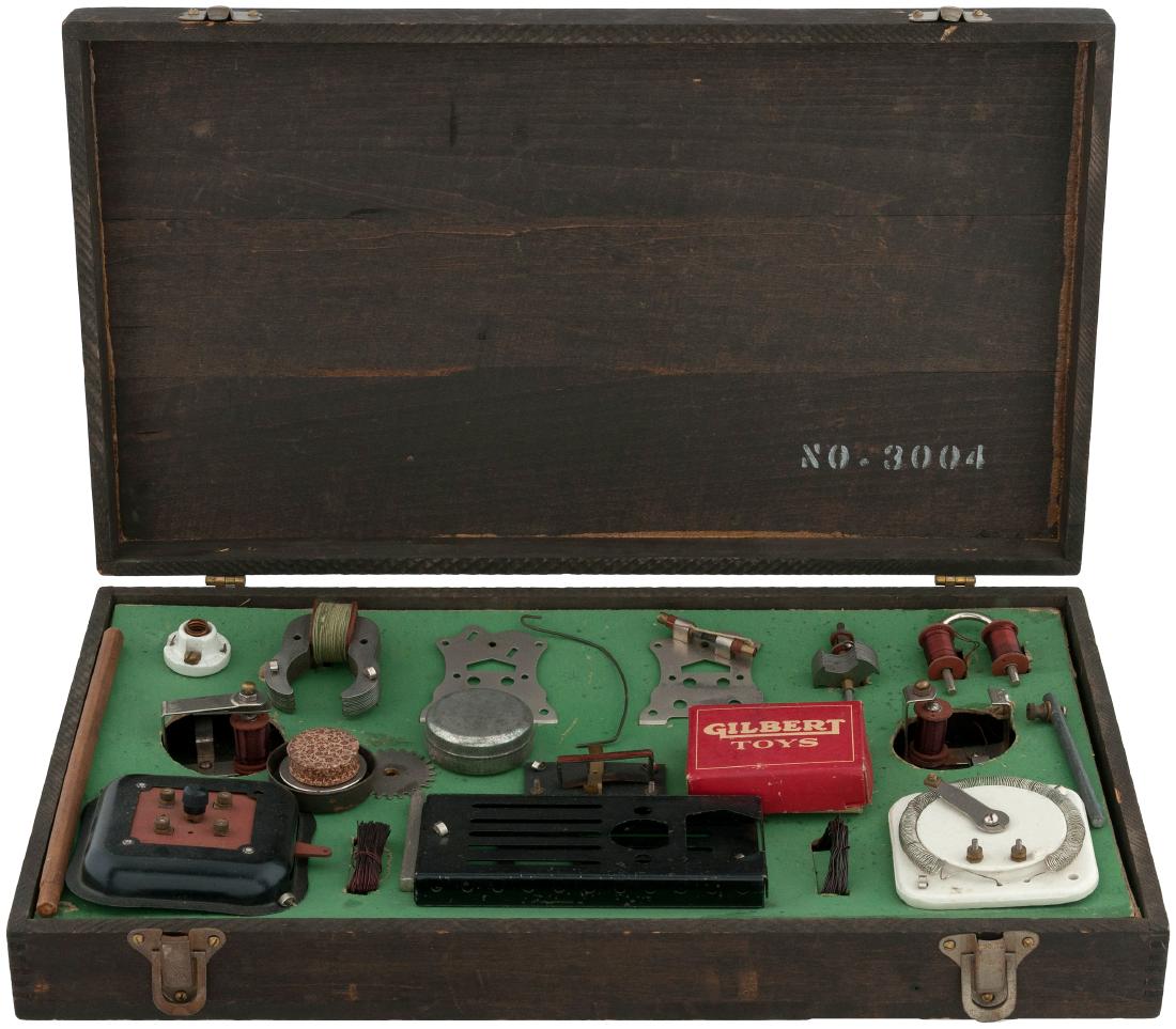 "GILBERT ELECTRICAL SET" BOXED 1921 SET.: 10-5/8x18.75x3.25" deep wooden case contains A.C. Gilbert Co. set No. 3004, 1921. Case has metal fasteners and lid has "Gilbert Toys Electrical" decal and this shows obvious wear. Underside of lid has