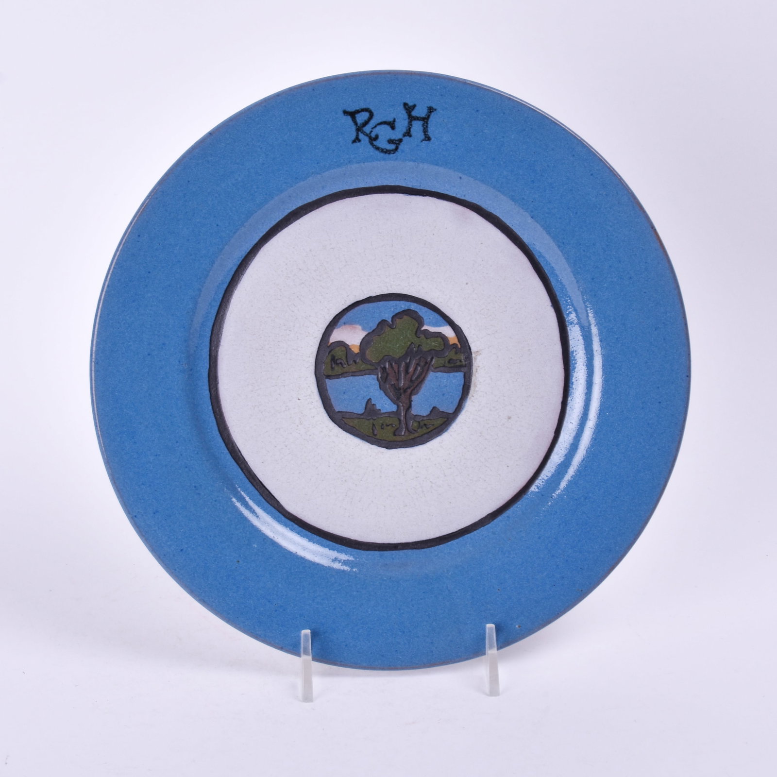 Saturday Evening Girls Plate: with a landscape medallion on a white and blue background; inscribed RGH. 5/8 inch high, 8 3/8 inches diameter, marked SEG/4-21/artist's cipher.