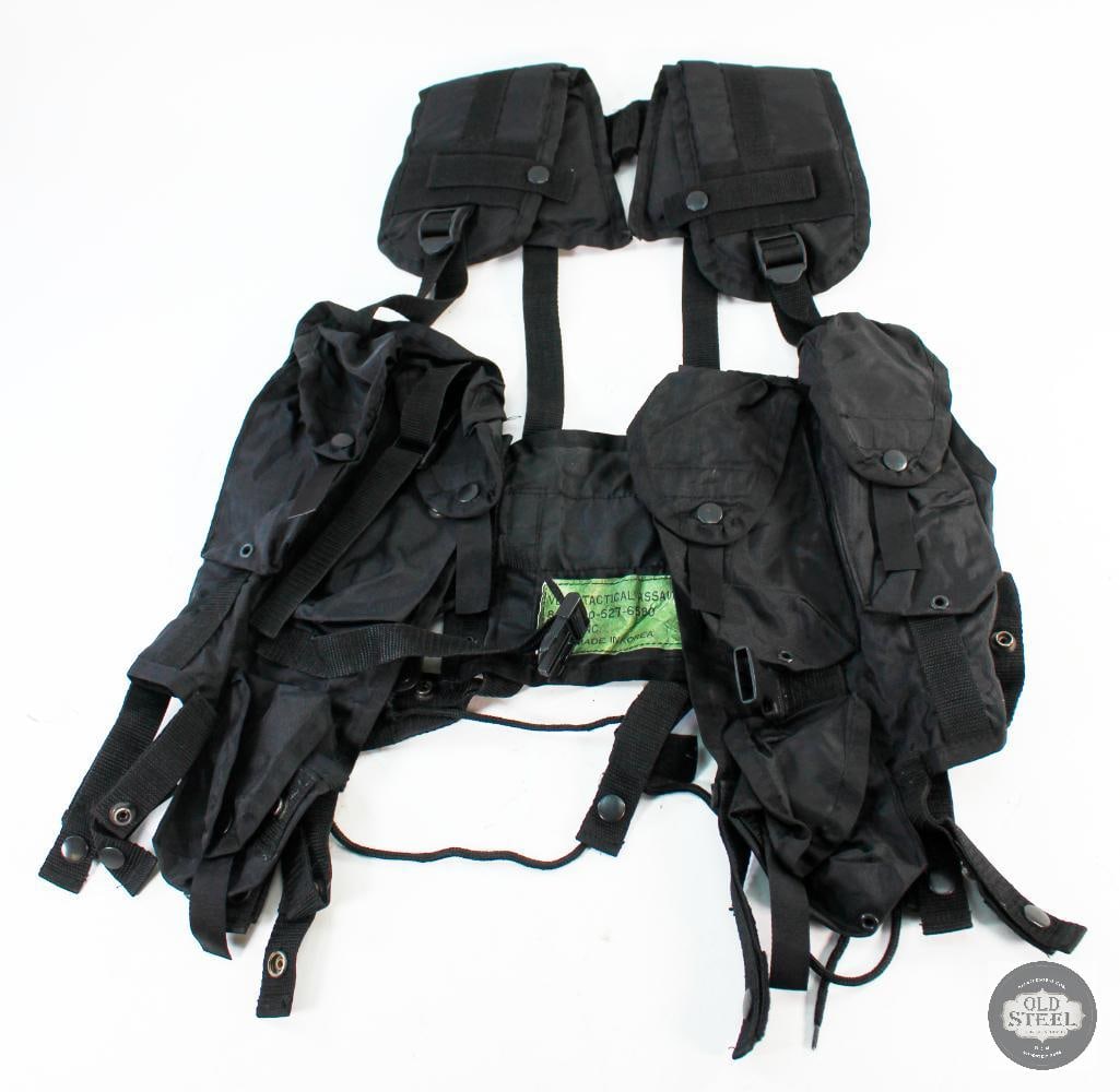 Black Nylon Chest Rig: A black nylon chest rig. The rig has 4 mag pouches, 2 on either side of the center connection and a grenade pouch on both sides. The rig has belt loops with snaps to secure over one's belt. The inside