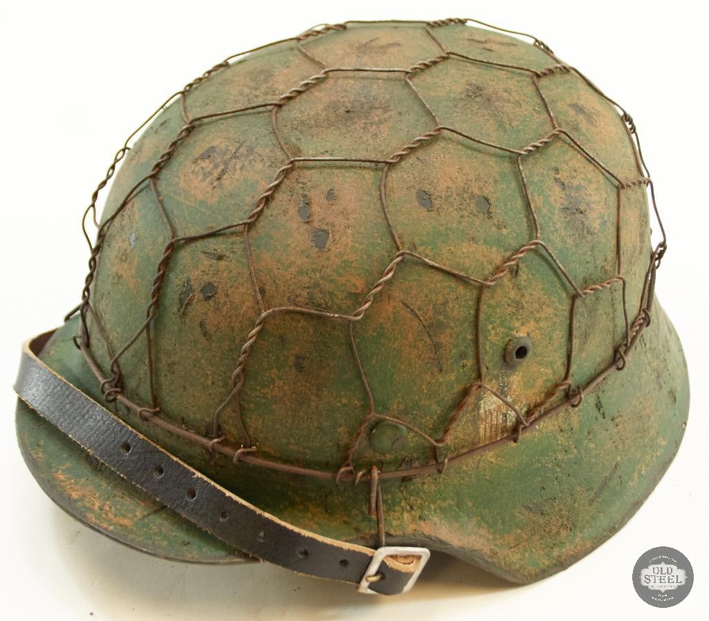 German M40 Stahlhelm with Liner: This lot contains a German M40 Stahlhelm with a liner and chinstrap, painted a mottled green and with a camo net. Professionally refurbished with original shell. 