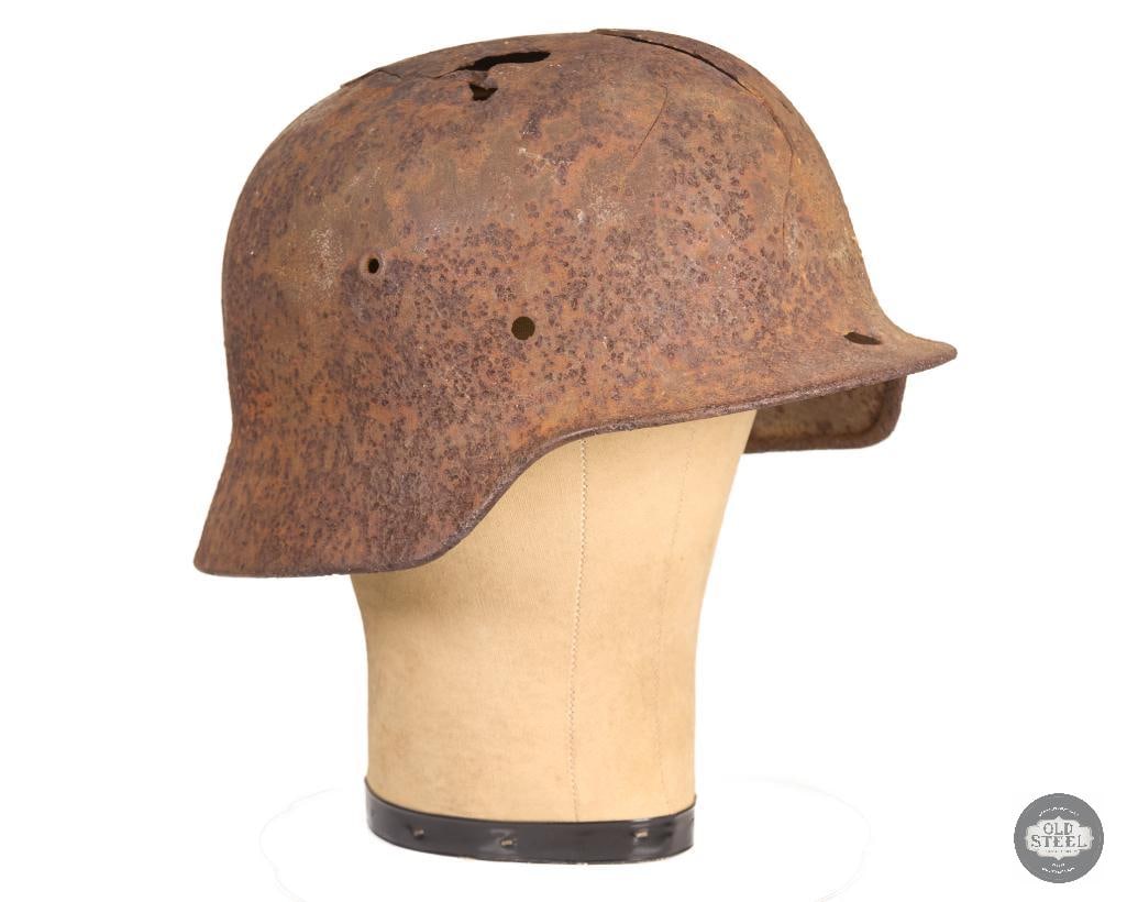 Original WWII German Stahlhelm Battlefield Recovery Helmet Relic Shell: This original WWII German Stahlhelm is a battlefield recovery relic shell exhibiting heavy oxidation, corrosion, and age-related wear. The shell has several holes and cracks resulting from prolonged e