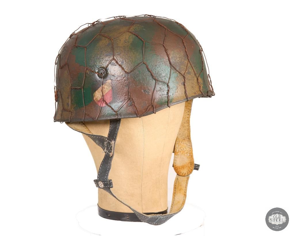 Original WWII German M38 Fallschirmjager Helmet Double Decal Camo Wire Display: This German M38 Fallschirmjager (paratrooper) helmet features an original shell with double decal markings and retains its liner. The helmet has been finished with a camouflage paint application and f