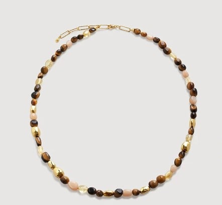 BEADED NECKLACE: BEADED NECKLACE Description: A slender necklace composed of alternating oval and rounded beads in warm earthy tones, including brown, honey, cream, and black, interspersed with several gold-toned