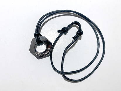 Pendentif YVES SAINT-LAURENT: Pendentif en forme d'écrou en métal marqué YVES SAINT LAURENT avec son cordon.