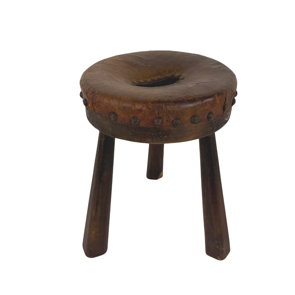 LEATHER AND WOOD TRIPOD MILK STOOL: Dimensions: H 14” x W 9.5”. Spanish Brutalist wooden tripod milking stool with studded leather seat.