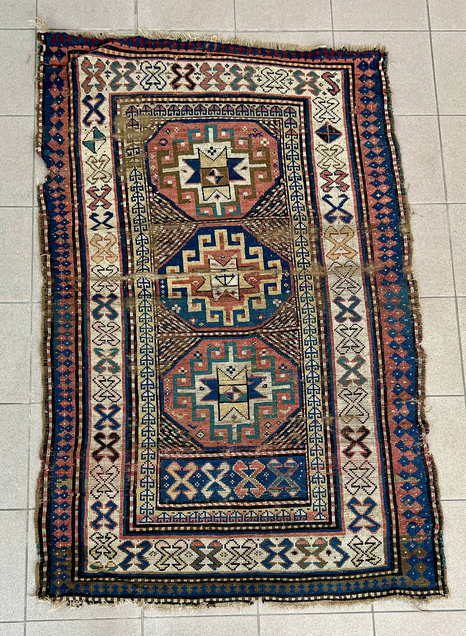 ANTIQUE MOUGHAN KAZAK RUG: Dimensions: H 5'9" x W 3'7". Distressed antique condition, rips and damages to edges, uneven wear.