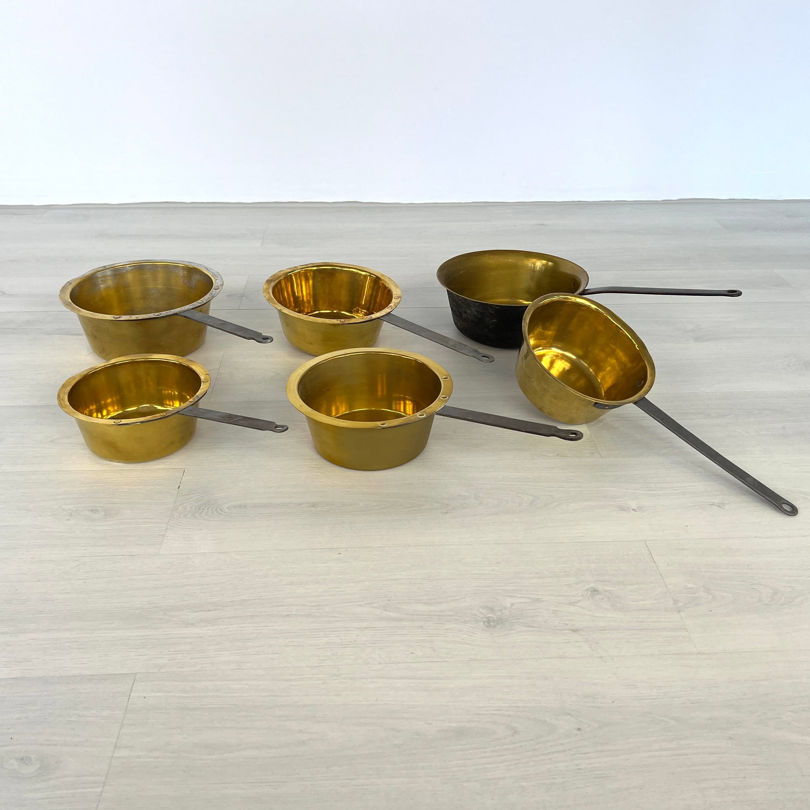 LOT 6 BRASS SAUCEPANS: Dimensions: H 4.5” x W 11.5”. Set of 6 Antique brass saucepans with iron handles. Dimensions: W 11.3"/11"/10.7"/10"/9.5".