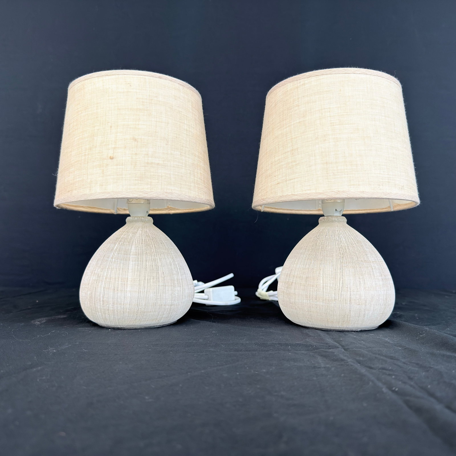 LUCIDE RAMZI TABLE LAMPS, A PAIR: Dimensions: H 10.5” x W 5”. Pair of Vintage Lucide Ramzi ceramic table lamps with light beige fabric lampshades.