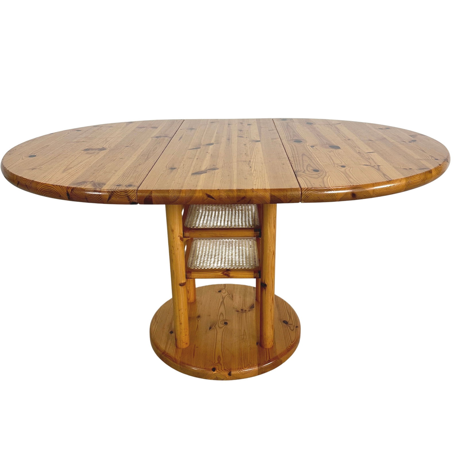EXTENDABLE DINING TABLE MANNER OF RAINER DAUMILLER: Dimensions: H 30.3” x W 42”. Vintage extendable pine dining table manner of Rainer Daumiller with two small rattan shelves. 1970s. Extended W 57”.