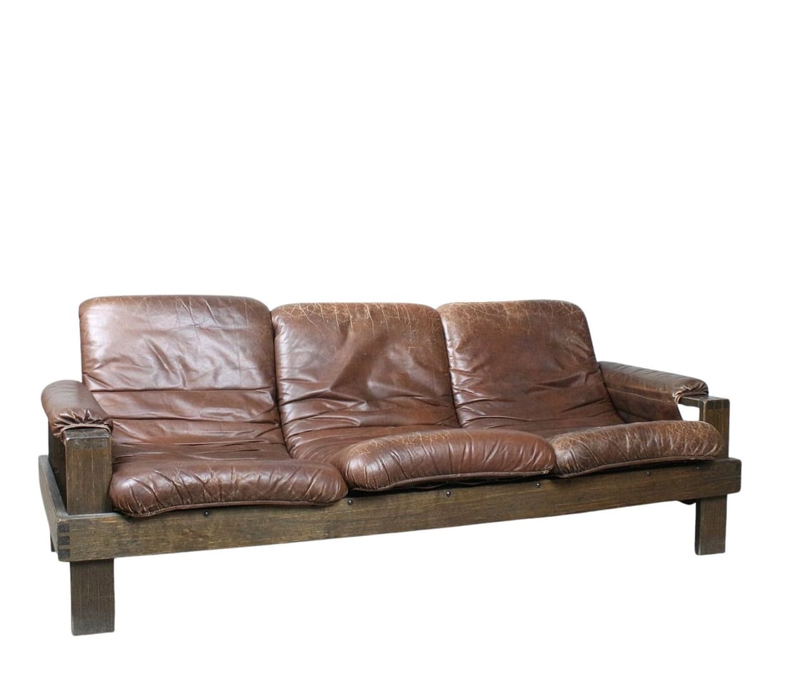 BRUTALIST SOFA MANNER OF ESKO PAJAMIES, 1970s: Dimensions: H 31.4” x W 82.6” x D 37.4” x SH 17.3”. Vintage Brutalist three-seater sofa manner of Esko Pajamies with brown leather cushions attached with leather straps and